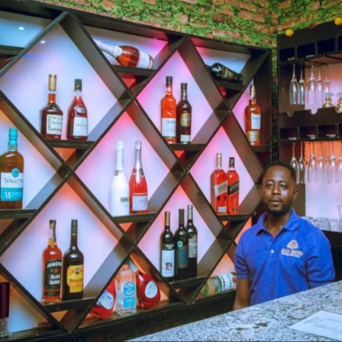 Barman in front of a lit diamond-shaped shelf of spirits and wine